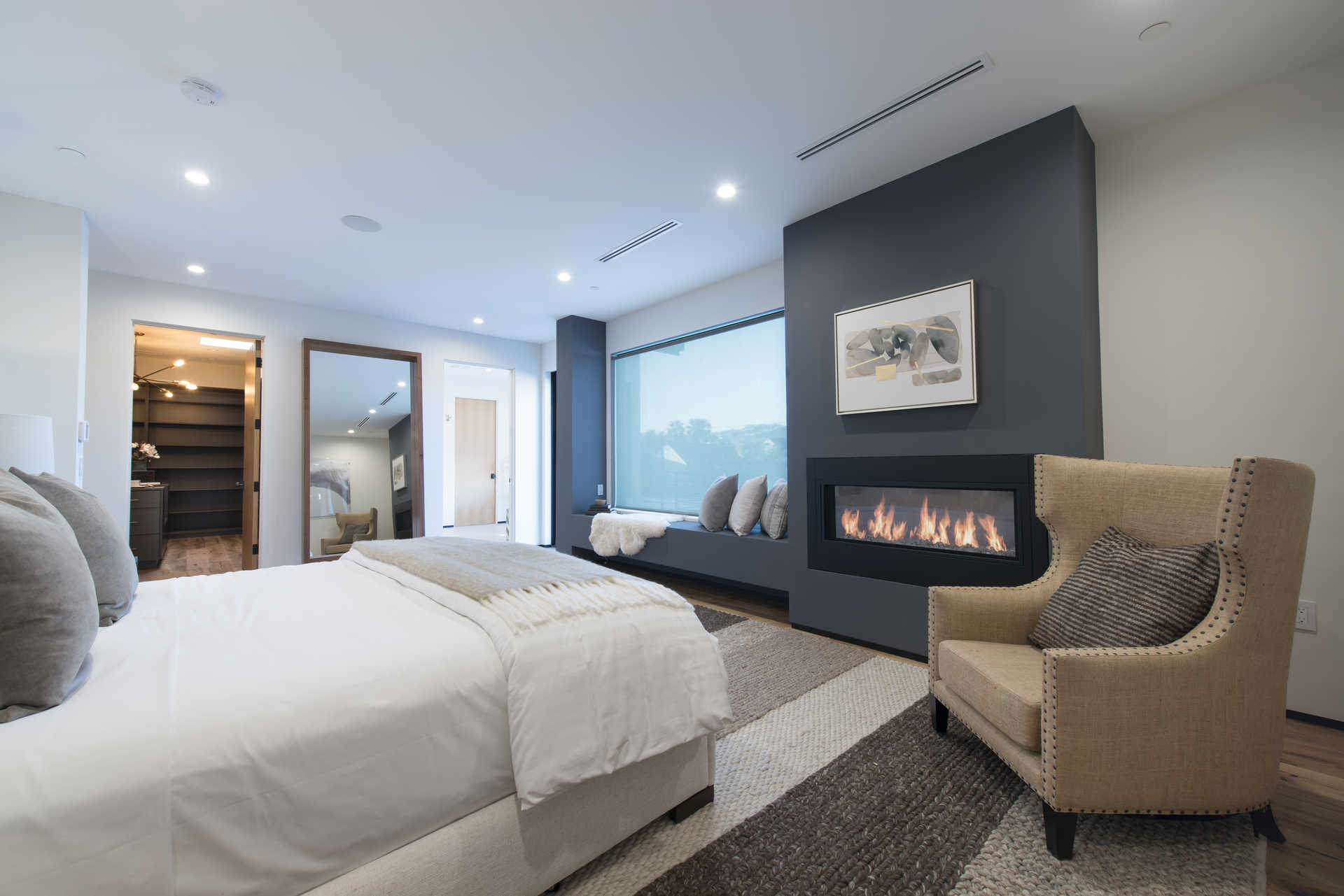 Primary bedroom with linear fireplace, custom millwork, and walk-in closet