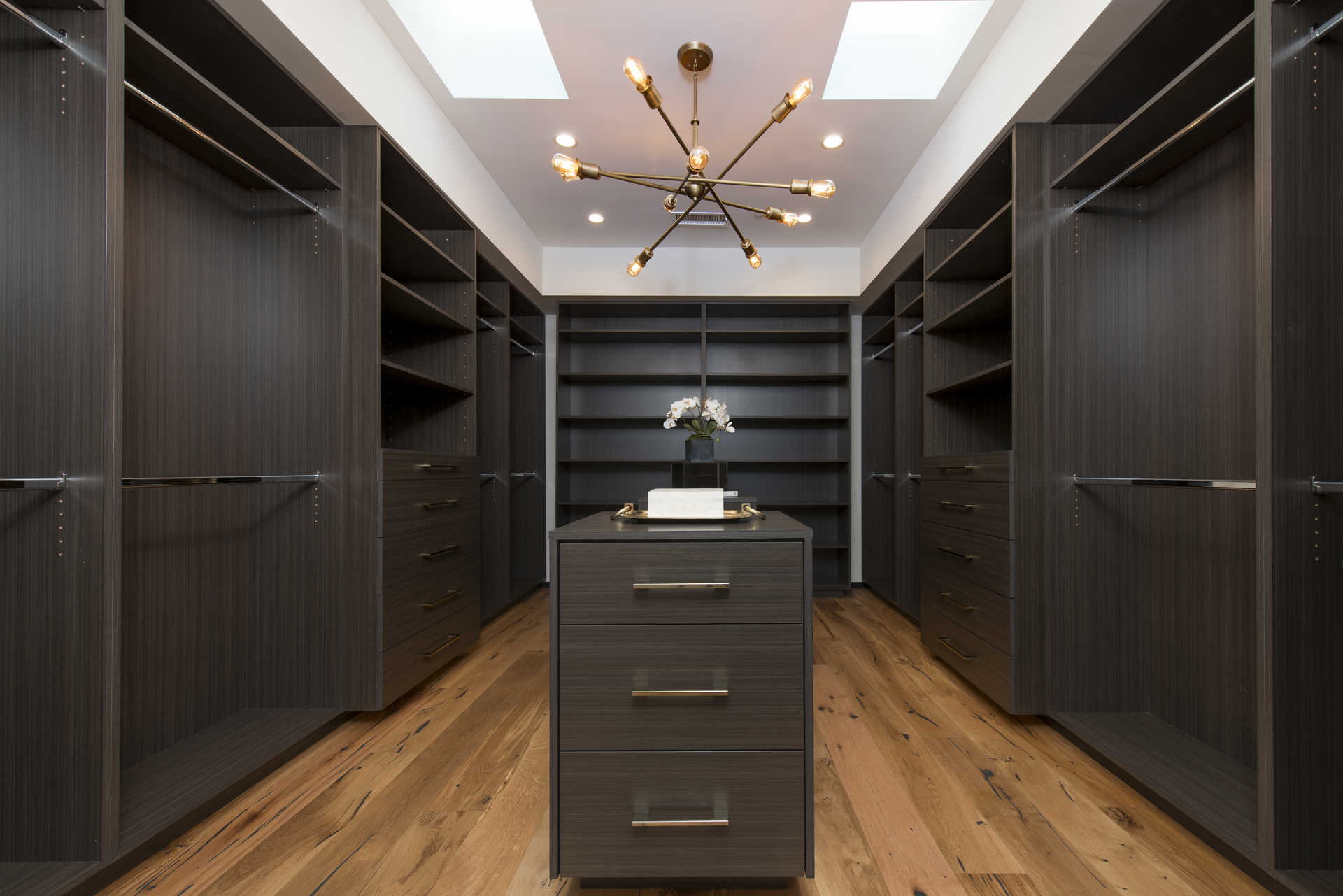 Walk-in primary closet with dark-stained millwork and brass hardware
